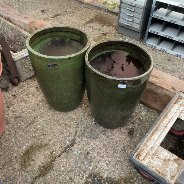 Two tall, green glazed garden pots in a garden setting.