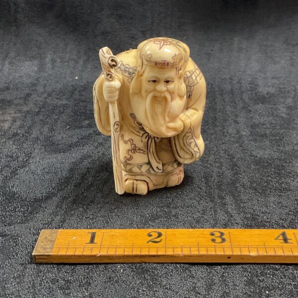 Antique Japanese bone sage figure with ruler for scale.
