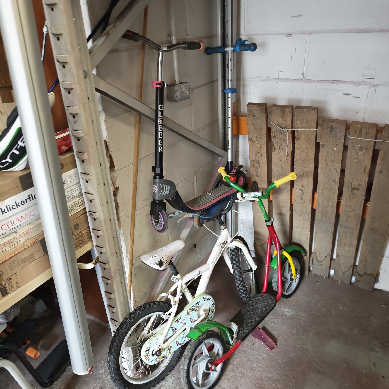 Kids scooters and a butterfly bicycle in a garage setting.