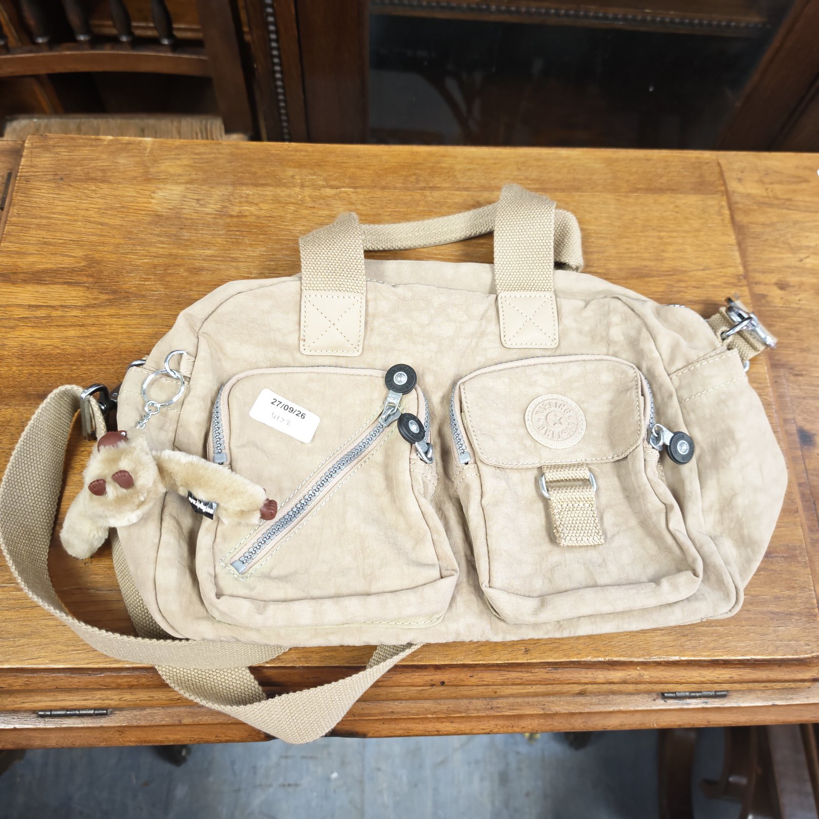 Beige Kipling ladies bag with monkey charm and adjustable strap.