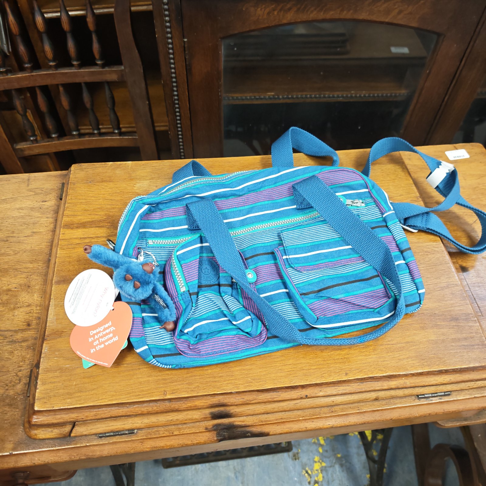 Unused Kipling ladies bag with vibrant striped pattern and shoulder strap.