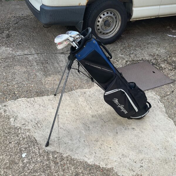Vintage MacGregor golf bag with assorted clubs on a street.