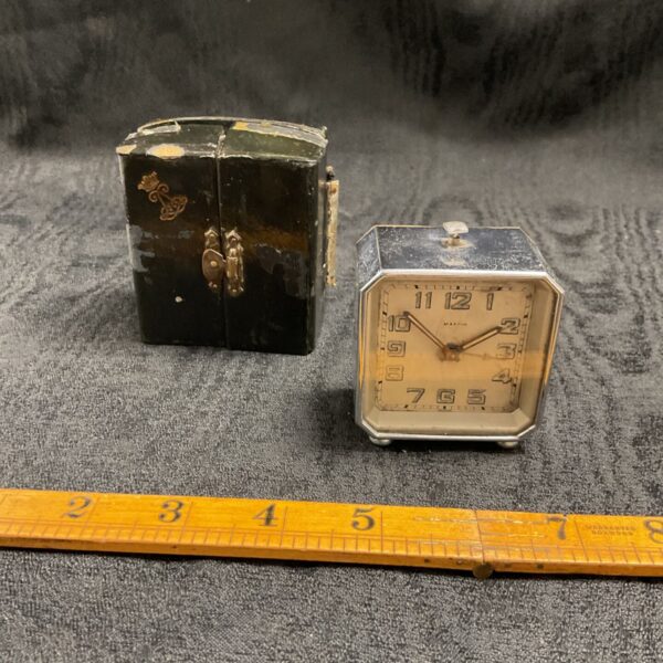 Antique Mappin travel clock with original case on grey fabric.