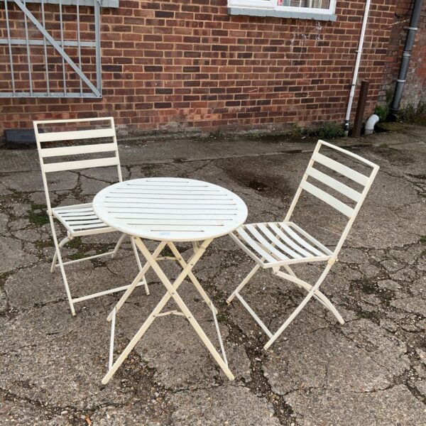 Metal garden table and two folding chairs in a backyard setting.