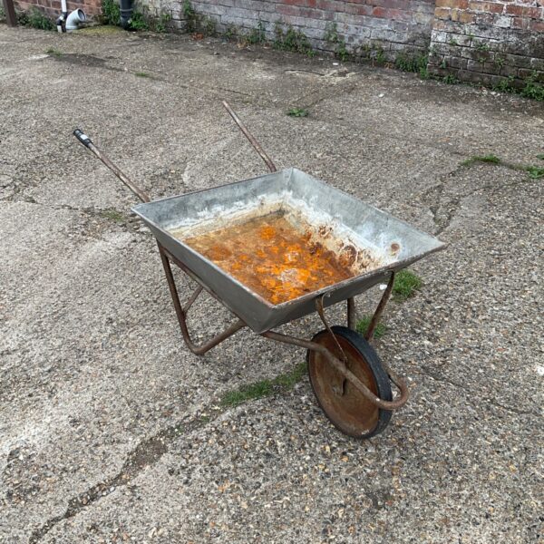 Weathered metal wheelbarrow in a garden setting.