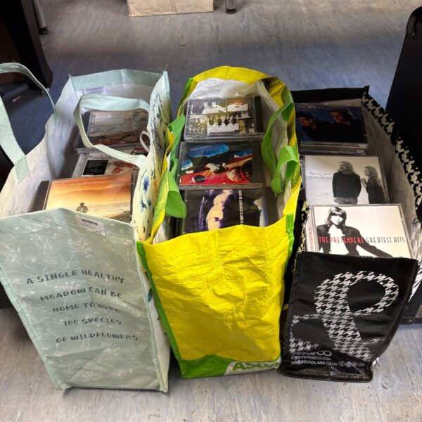 Three bags filled with a diverse music CD collection.