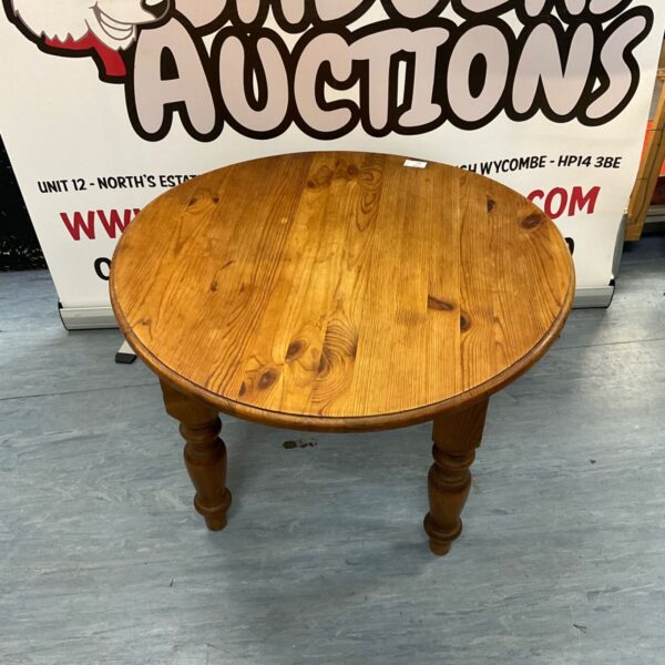 Small round pine coffee table with a warped top and turned legs.