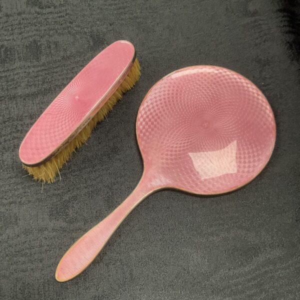 Vintage pink guilloche enamel hand mirror and brush set on grey fabric.