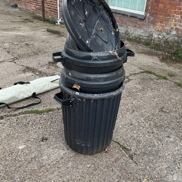 Lot of three dark plastic dustbins with lids outdoors.