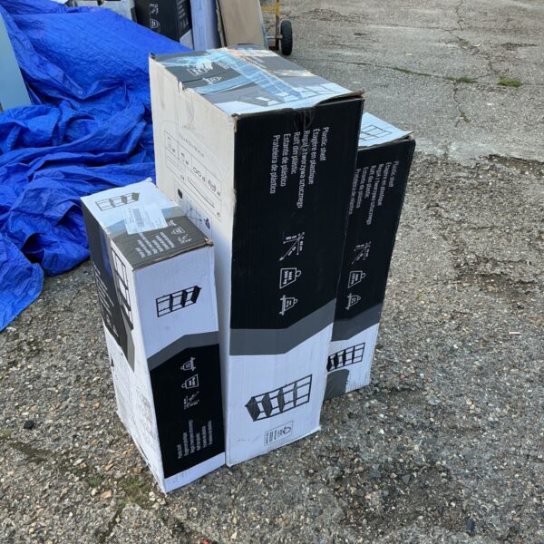 Three boxes of unopened plastic shelving units for storage.