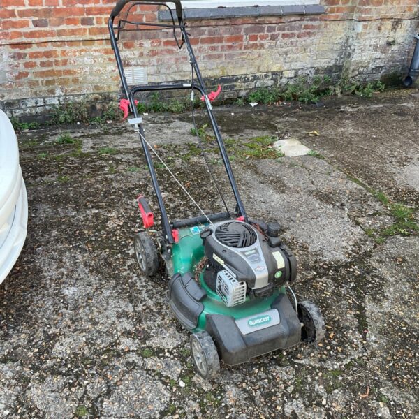Vintage Qualcast petrol lawnmower in a garden setting.