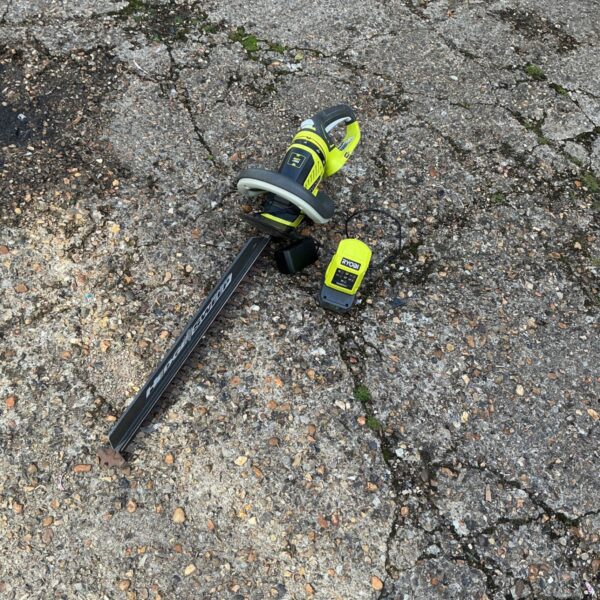 Ryobi cordless hedge trimmer with battery and charger for garden maintenance.