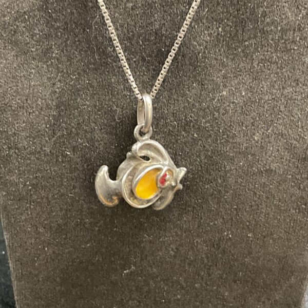 Close-up of silver fish pendant with yellow and red enamel details.