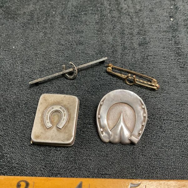 Antique silver horse shoe brooches and locket on dark background.