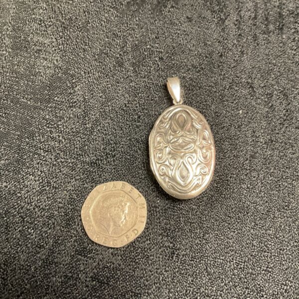 Silver hinged locket displayed with a coin for scale.