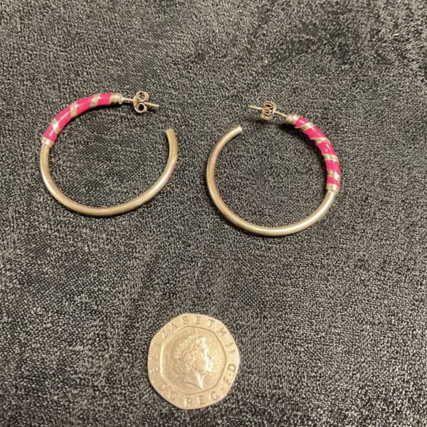 Close-up of silver hoop earrings with pink enamel detail.