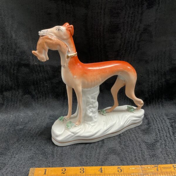 Antique Staffordshire greyhound figure with hare in mouth, side view.