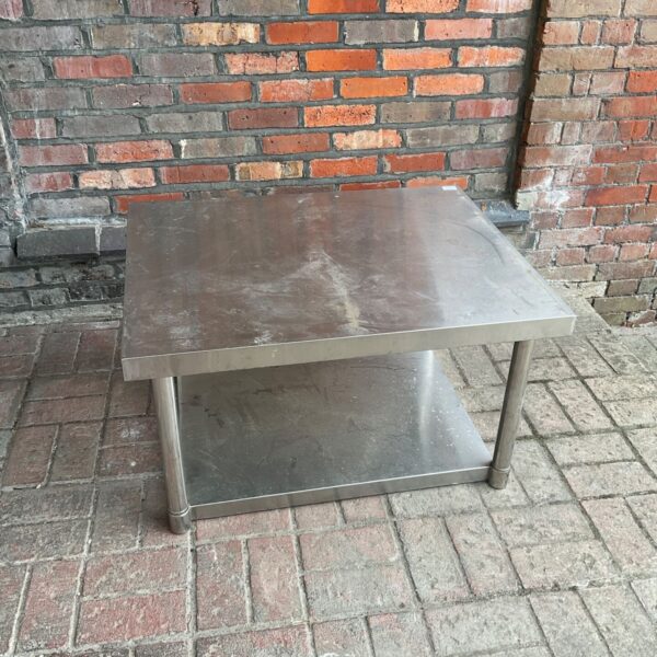 Stainless steel industrial table with lower shelf, showing signs of wear.