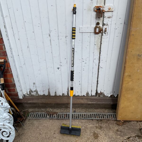 Used telescopic garden broom leaning against a white door.