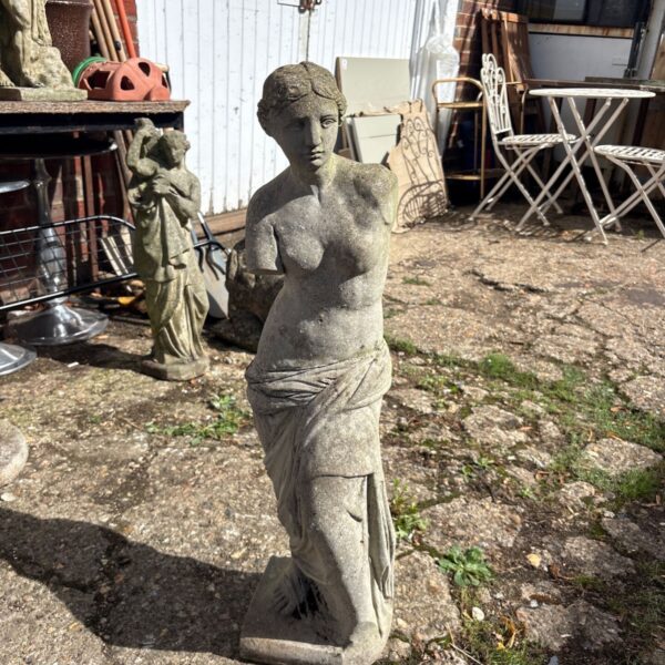 Stone Venus de Milo statue in a garden setting.