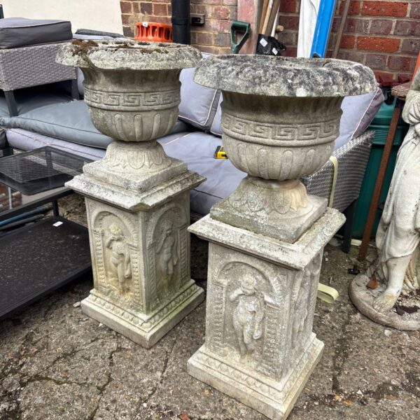 Pair of weathered Victorian garden urns with plinths in a garden setting.