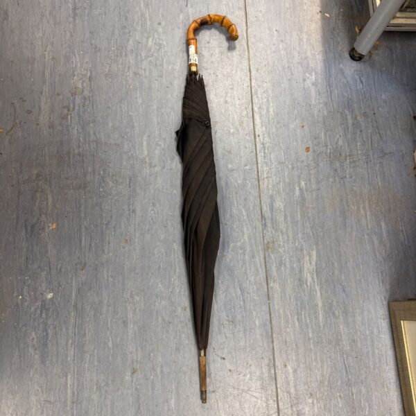 Vintage black umbrella with a bamboo handle, displayed indoors.