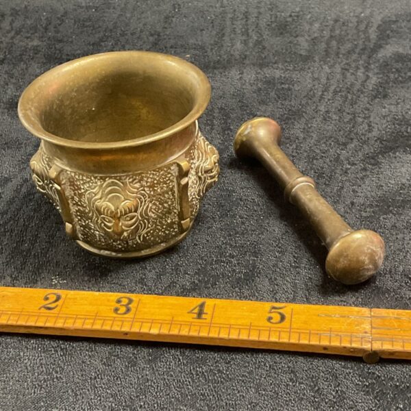 Vintage brass mortar and pestle with lion head decoration.