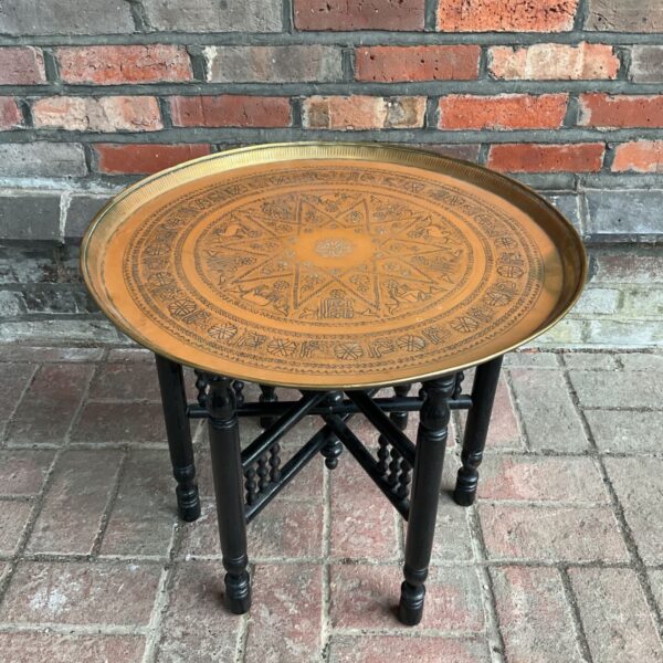 Vintage brass tray table with ornate arabesque design and black legs.