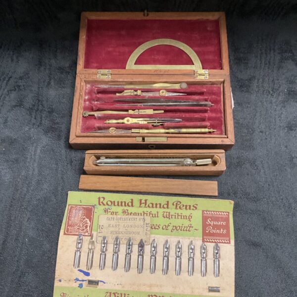 Vintage drawing instrument set in wooden box with compass and pen nibs.