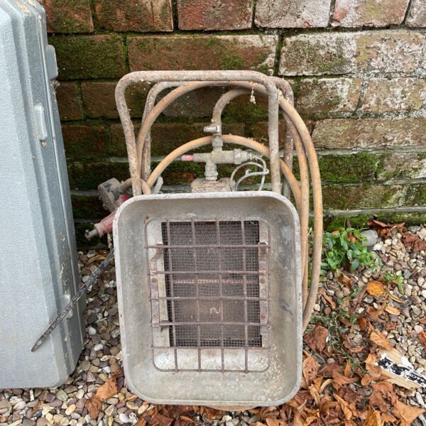 Vintage gas workshop heater with metal cage and gas lines.