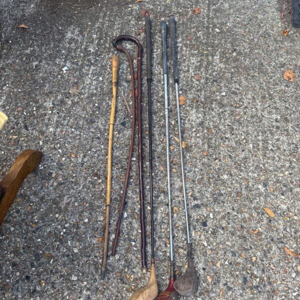 Vintage golf clubs and walking sticks laid out on pavement.