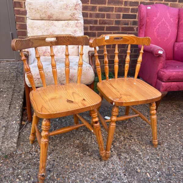 Two vintage pine chairs with spindle backs in a rustic setting.