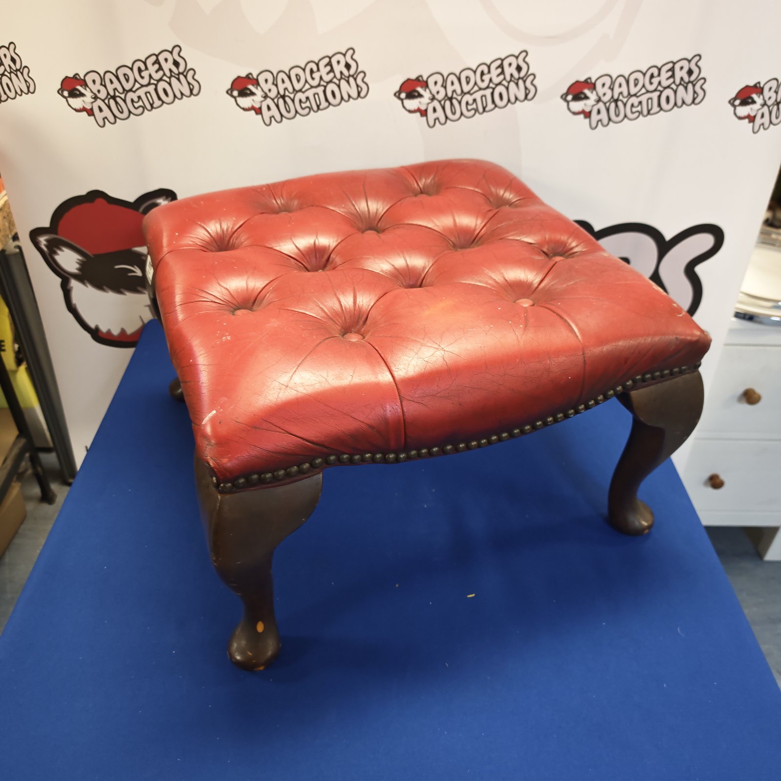 Vintage red leather footstool with button detailing and wooden legs.