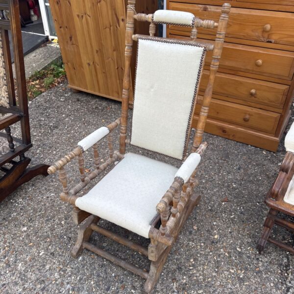 Vintage mechanical rocking chair with spindle back and worn upholstery.