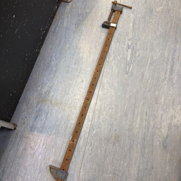 Long vintage metal sash clamp on a grey floor.