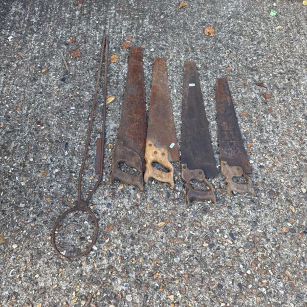 Vintage wood saws and antique pottery tongs on gravel surface.