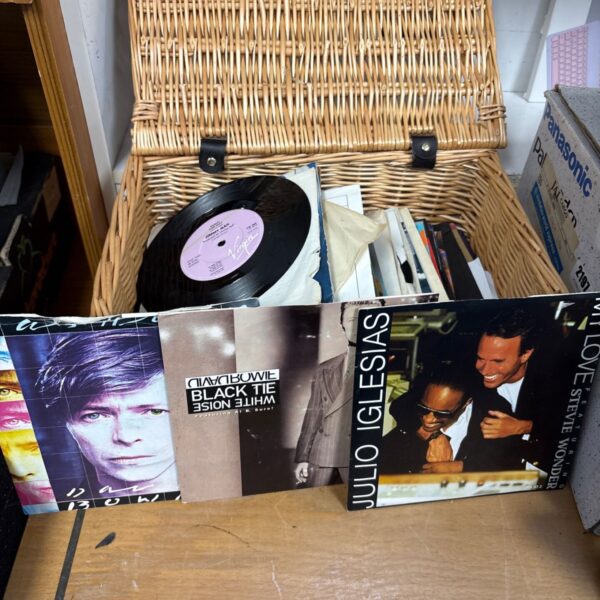Mixed vinyl record collection in a wicker basket, including David Bowie.