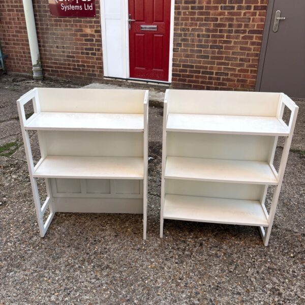 Two white folding shelves against a brick wall.