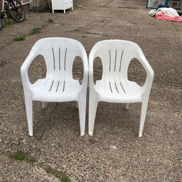 Two white plastic garden chairs in a garden setting.