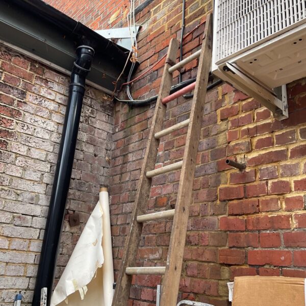 Vintage wooden ladder leaning against brick wall in garden.