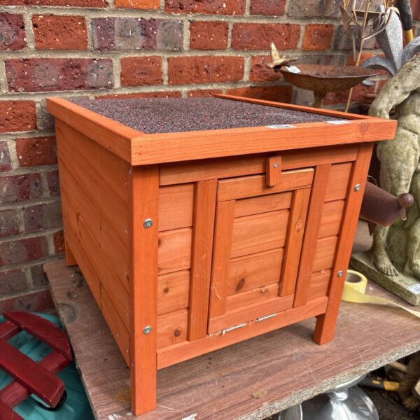 Wooden pet shelter against a brick wall in a garden setting.