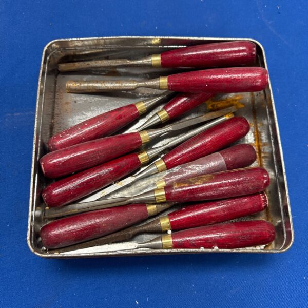 Vintage woodworking chisels with wooden handles in a metal tray.