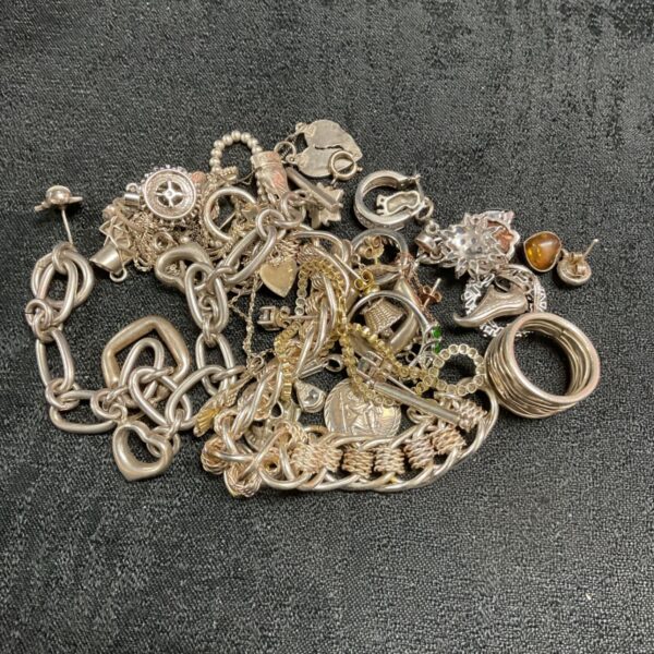 Tangled collection of 925 silver bracelets, charms and earrings on dark surface