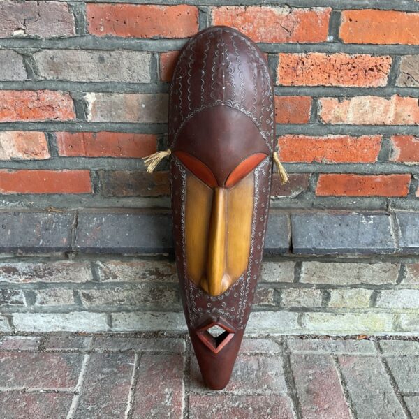 Large African tribal mask with intricate carvings on a dark wood background.