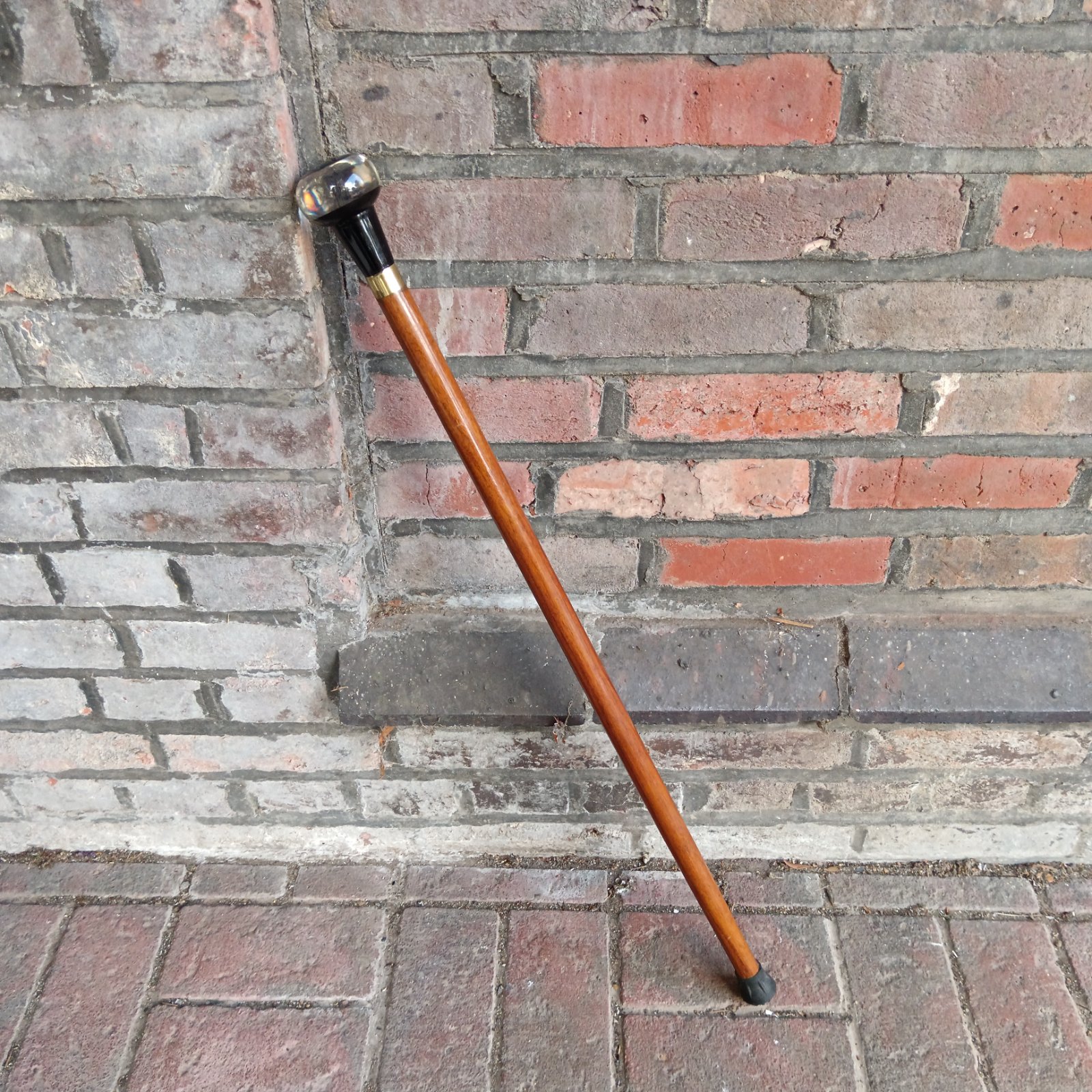 Antique walking cane with a detailed dragonfly knop against a brick wall.