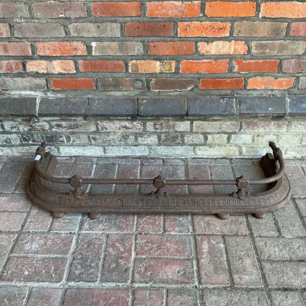 Antique cast iron fireplace fender with ornate floral design.