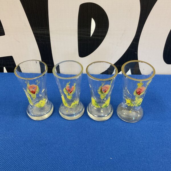 Antique hand painted shot glasses with floral designs on display.