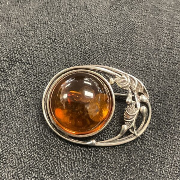 Art Nouveau silver brooch with amber stone, detailed floral design.
