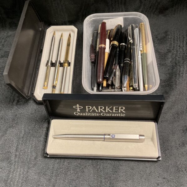 Assorted pens in a tub, including Parker brand examples.