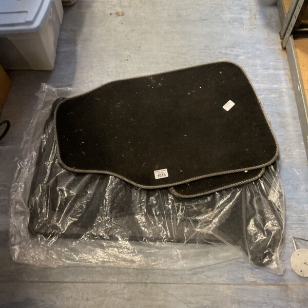 Three black carpet car floor mats with grey edging on blue-grey floor
